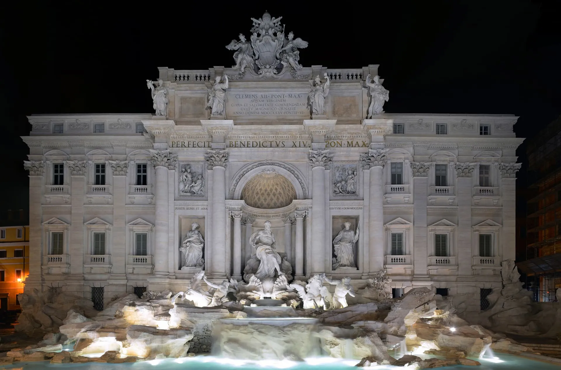 Trevi Fountain floodlit at night, Neptune's chariot reflected in calm water.